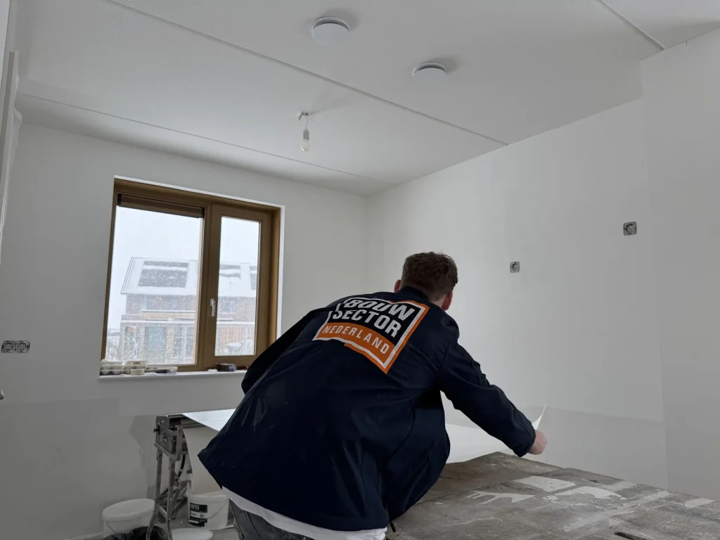 Behanger in donkerblauwe werkjas van Bouwsector Nederland pakt een baan van de plaktafel