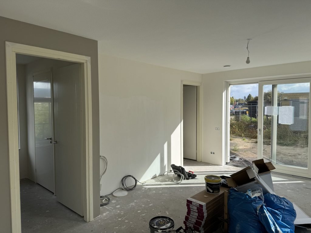 Woonkamer met open deuren naar de gang en een slaapkamer, de wanden klaar voor het behang