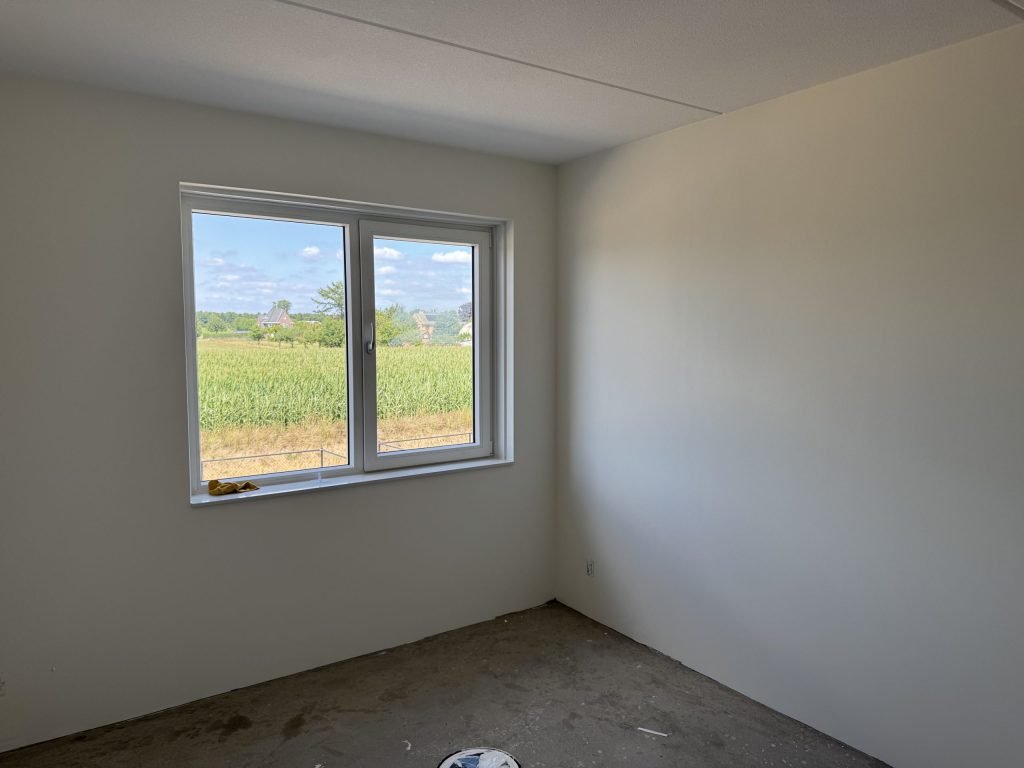 Kamer met gladde lichte wanden en een raam met uitzicht over de velden