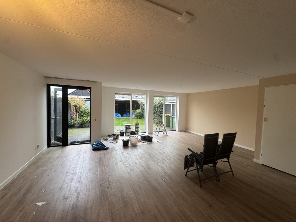 Ruime woonkamer met tuindeuren, lichte wanden en verfemmers op de vloer tijdens het werk