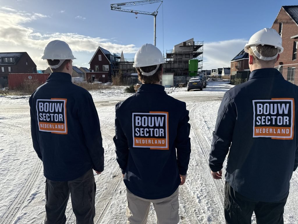 Drie vakmensen van Bouwsector Nederland met witte helm en logo op de jas kijken naar woningen in aanbouw