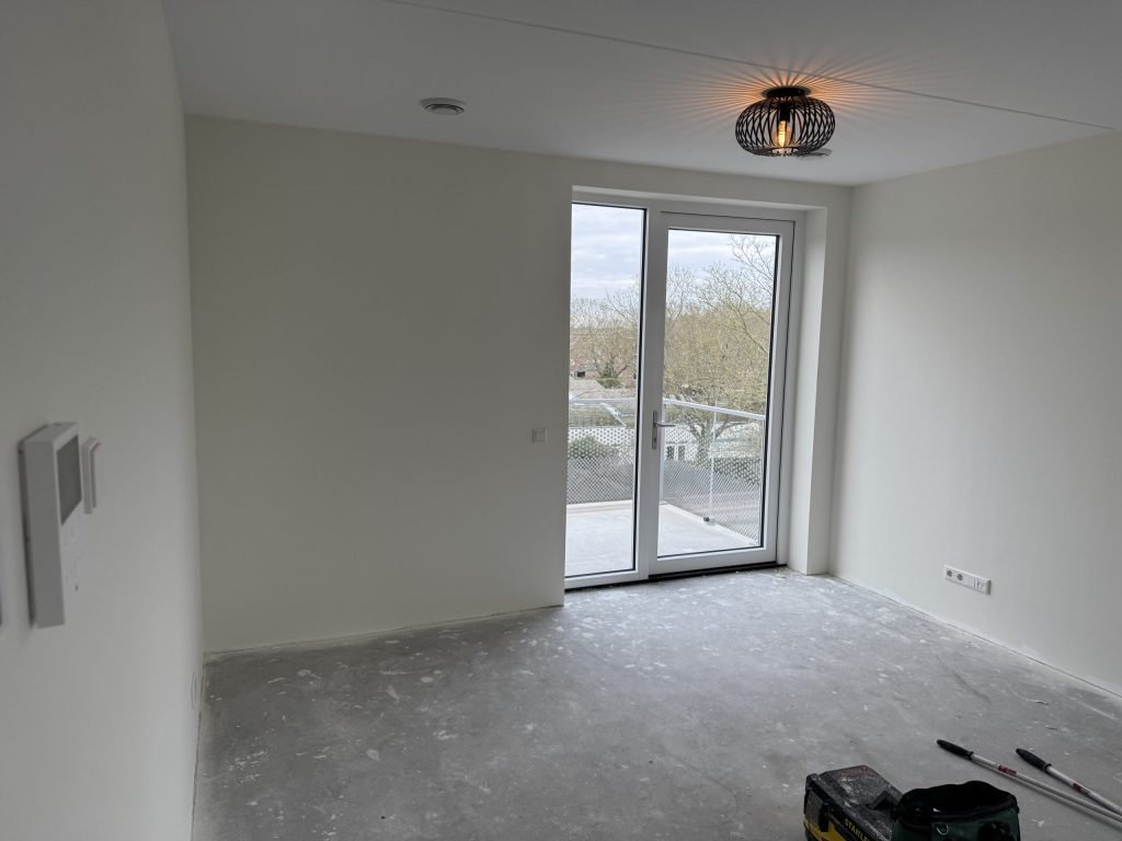 Lege nieuwbouwkamer met witte wanden en openslaande deuren, kort na de oplevering